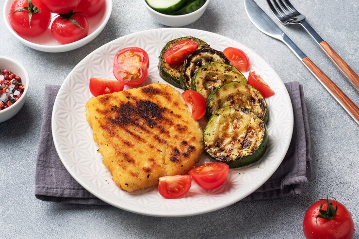 Schnitzel de pollo y calabacín cocinado a la parrilla. Tomates frescos en un plato. Listo deliciosa cena almuerzo.