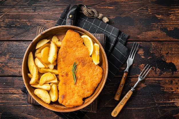 Schnitzel de weiner frito austriaco con gajos de patata en un plato de madera Fondo de madera Vista superior