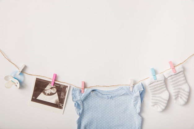 Schnuller; ultraschallbild; socken; babykleidung, die an der wäscheleine über weißem hintergrund hängt