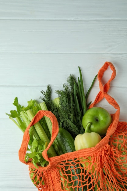 Schnurbeutel mit grünem Gemüse auf weißem hölzernem Hintergrund