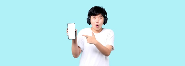 Schock- und Überraschungsgesicht des Tomboy-Asiaten, der Smartphone und Kopfhörer auf blauem Hintergrund präsentiert