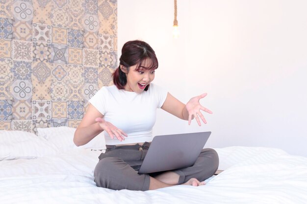 Schockieren Sie asiatisches schönes Mädchen, arbeiten Sie mit dem Laptop im Bett. Arbeiten Sie von zu Hause aus