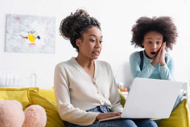 Schockierte afroamerikanische Mutter und Tochter, die zu Hause auf den Laptop schauen