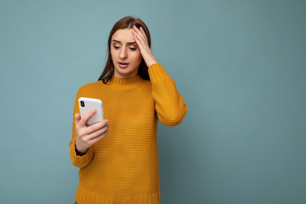 Schockierte attraktive positive junge Frau, die orange Pullover trägt