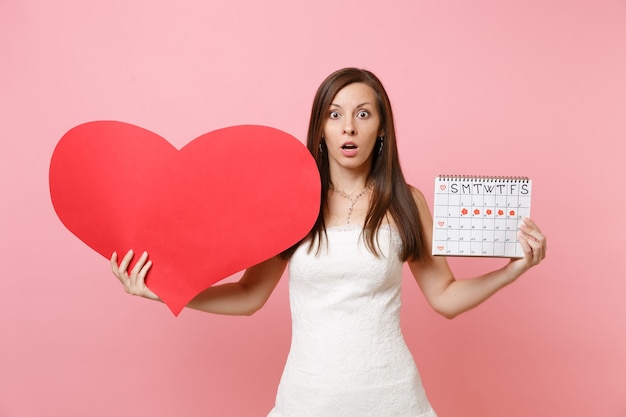 Schockierte Frau im weißen Kleid, die einen leeren, leeren, roten, weiblichen Periodenkalender zur Überprüfung der Menstruationstage hält