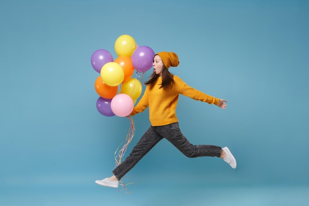 Schockierte junge Frau Mädchen in Pullover und Hut posiert isoliert auf blauem Hintergrund. Geburtstagsfeier, Menschen Emotionen Konzept. Mock-up-Kopienbereich. Feiern halten bunte Luftballons springen.