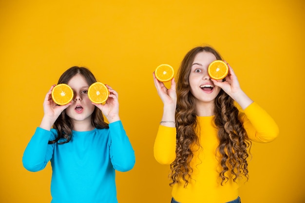 Schockierte Teenager-Mädchen halten Orangenfrüchte auf gelbem Hintergrund