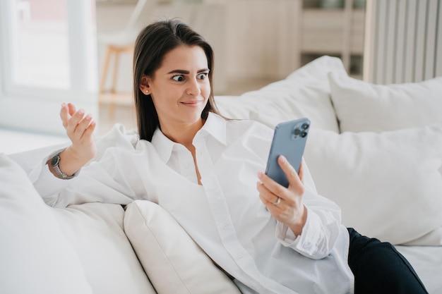 Foto schockierte, überraschte hispanische junge frau im weißen hemd, die mit verblüfftem gesichtsausdruck mit freunden spricht