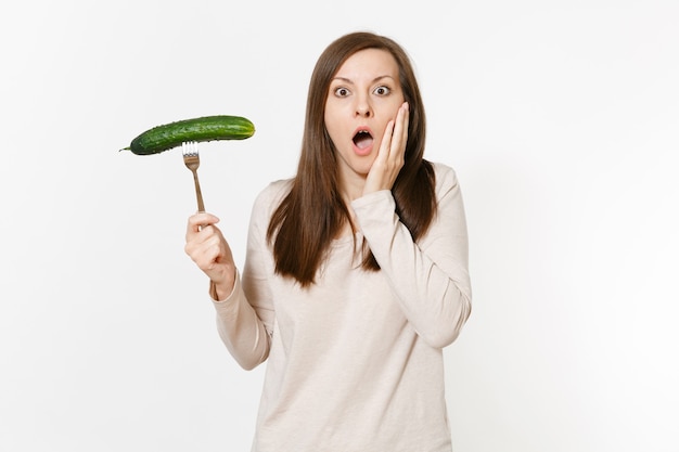 Schockierte Veganerin hält in der Hand grüne frische Gurken auf der Gabel isoliert auf weißem Hintergrund. Richtige Ernährung, vegetarisches Essen, gesunder Lebensstil, Gemüsekonzept. Werbefläche mit Kopienraum.