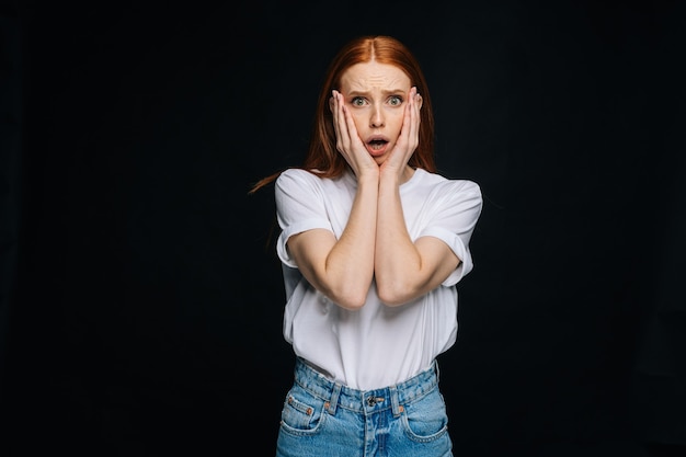 Schockierte verängstigte junge Frau, die ein T-Shirt und eine Jeanshose trägt, die mit offenem Mund steht