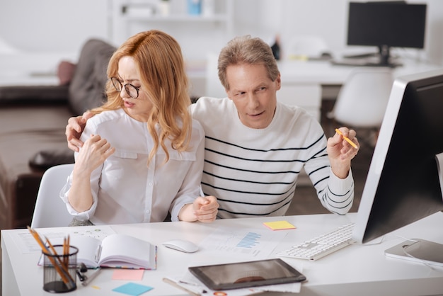 Schockierte wütende junge Sekretärin, die im Büro sitzt und an dem Projekt arbeitet, während sie ihre Empörung über das Verhalten des Chefs zum Ausdruck bringt