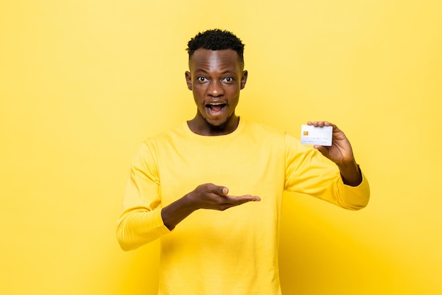 Schockierter afrikanischer Mann in Freizeitkleidung mit Kreditkarte auf gelbem Studiohintergrund