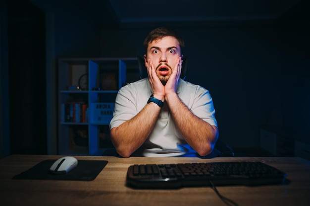 Schockierter Freiberufler mit Bart benutzt nachts einen Computer im Schlafzimmer und schaut auf den Bildschirm