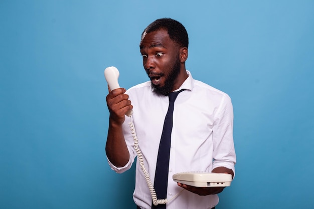 Schockierter Geschäftsmann blickt ehrfürchtig auf den Empfänger des Schnurtelefons, nachdem er den Streit mit einer am anderen Ende der Leitung schreienden Person verloren hat. Büroangestellter mit Telefon kann nicht glauben, was er hört.