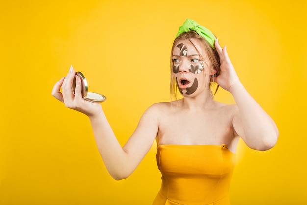 Schockierter Grill mit Fleck auf dem Gesicht isoliert an der gelben Wand. Gestresste Frauen mit schlechter Hautroutine