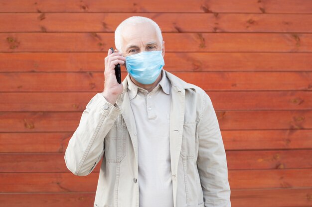 Schockierter Mann mit medizinischer Gesichtsmaske, der das Telefon benutzt, um nach Nachrichten zu suchen