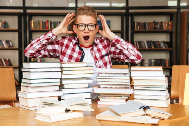 Schockierter Teenager, der am Bibliothekstisch sitzt