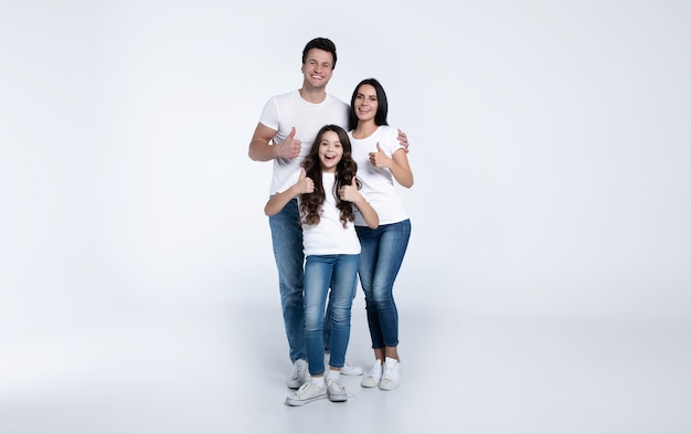 Schön aufgeregt und das lustige Familienteam posiert in einem weißen T-Shirt, während sie im Studio auf weißem Hintergrund isoliert sind.