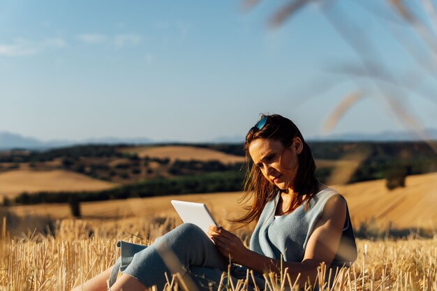 Schöne 40-jährige Frau liest Tablet auf dem Feld. Entspannen Sie Sich. Kultur. Freizeit, psychiatrische Betreuung