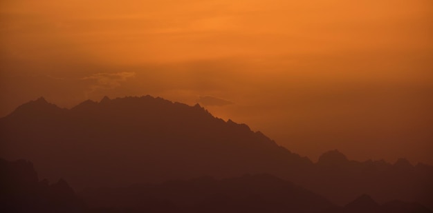 Schöne abendliche Panoramalandschaft mit heller untergehender Sonne über fernen Berggipfeln bei Sonnenuntergang