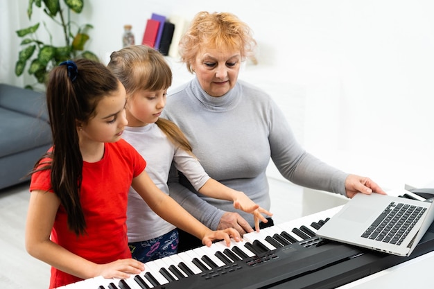 Schöne ältere Frau bringt kleinen Enkelkindern bei, Synthesizer zu spielen. Die junge Großmutter spielt Klavier für ihre Enkelkinder.