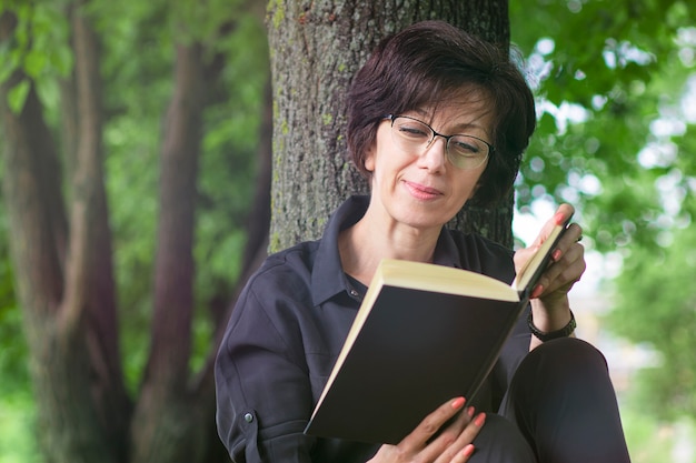 Schöne ältere Frau, die auf dem Boden sitzt und Buch liest