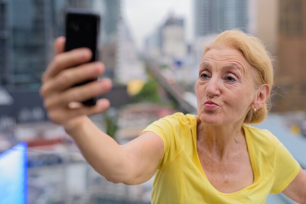 Schöne ältere Frau, die selfie mit Handy in der Stadt nimmt