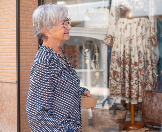 Schöne ältere Frau, die sich das Schaufenster ansieht Ältere weißhaarige Dame, die in Mode gekleidet ist und das Einkaufen genießt