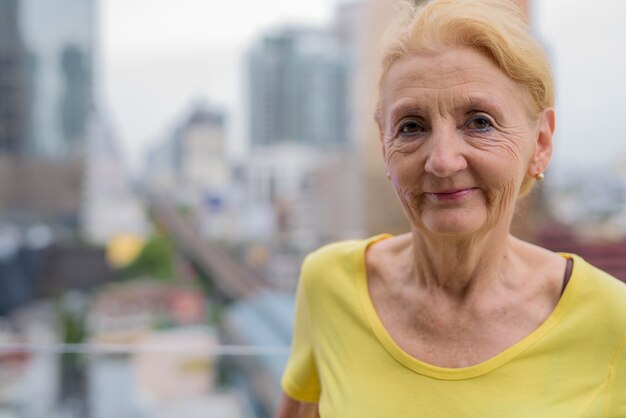 Schöne ältere Frau mit blondem Haar auf Ansicht der Stadt