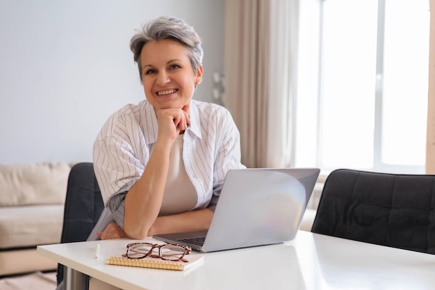 Schöne ältere Frau, Rentnerin, Geschäftsfrau mit grauen Haaren, arbeitet aus der Ferne am Computer.