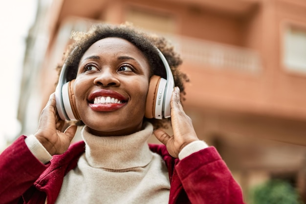 Schöne afrikanisch-amerikanische Frau mit Afro-Haar lächelt glücklich und selbstbewusst und trägt Kopfhörer, die Musik hören