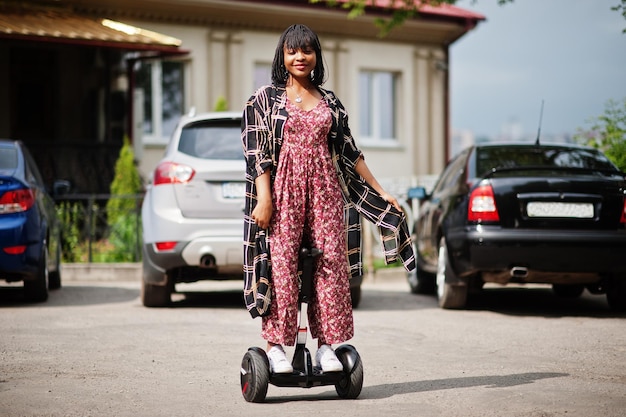 Schöne afrikanisch-amerikanische Frau mit Segway oder Hoverboard Schwarzes Mädchen auf zweirädrigem, selbstausgleichendem Elektroroller gegen Parkplatz