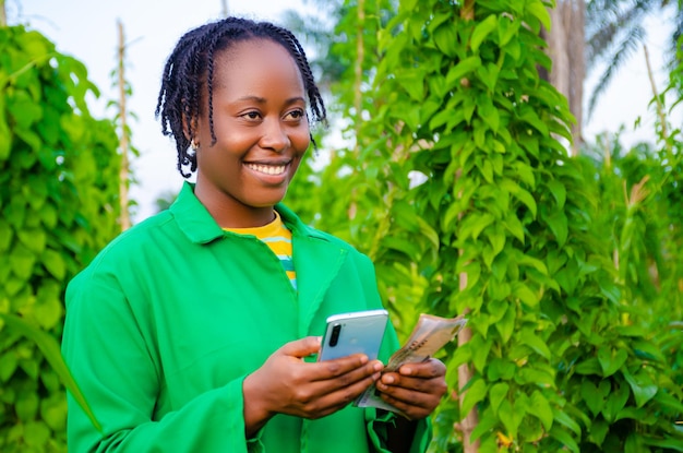 Schöne afrikanische dame auf der farm, die sich aufgeregt fühlt, als sie ihr telefon und geld hält