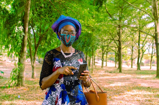 Schöne afrikanische Frau im Freien mit Gesichtsmaske, die auf ihr Telefon zeigt