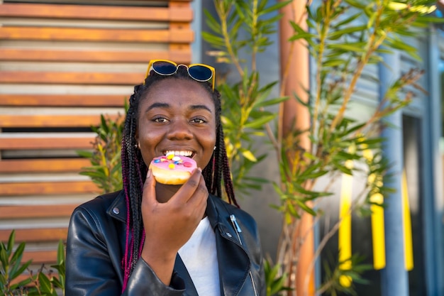 Schöne afrikanische Frau isst einen bunten Donut