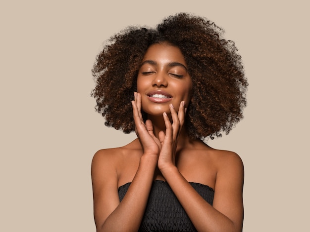 Schöne afrikanische Frau schwarzes T-Shirt Porträt Afro-Haarschnitt, der ihr Gesicht berührt Farbhintergrund braun