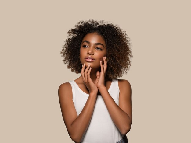 Schöne afrikanische Frau weißes T-Shirt Porträt Afro-Haarschnitt, der ihr Gesicht berührt Farbhintergrund braun