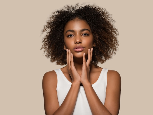 Schöne afrikanische Frau weißes T-Shirt Porträt Afro-Haarschnitt, der ihr Gesicht berührt Farbhintergrund braun