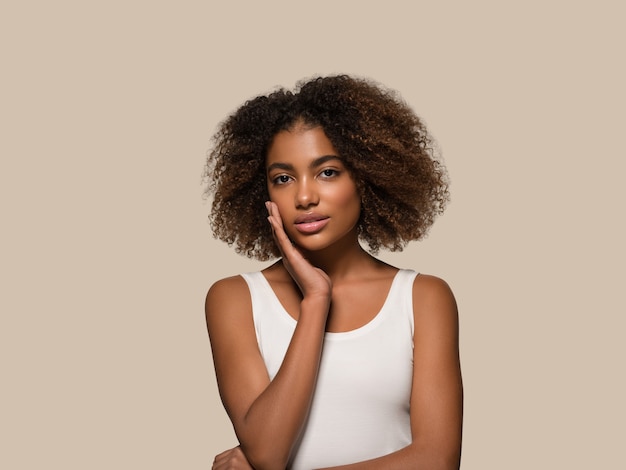 Schöne afrikanische Frau weißes T-Shirt Porträt Afro-Haarschnitt, der ihr Gesicht berührt Farbhintergrund braun