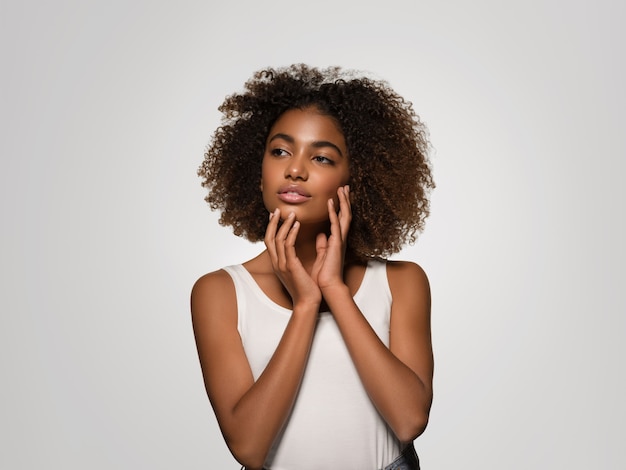 Schöne afrikanische Frau weißes T-Shirt Porträt Afro-Haarschnitt, der ihr Gesicht berührt Farbhintergrund grau