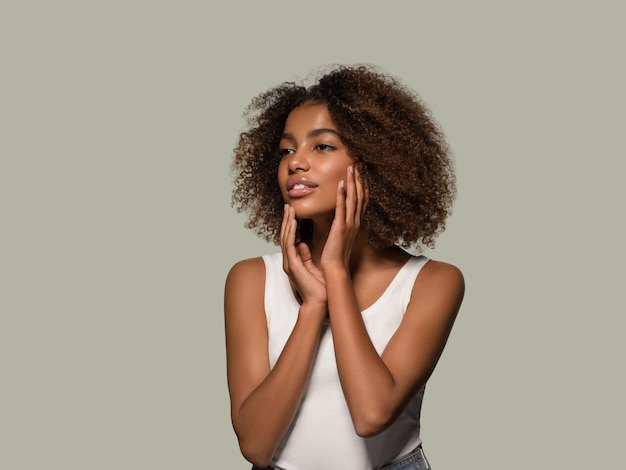 Schöne afrikanische Frau weißes T-Shirt Porträt Afro-Haarschnitt, der ihr Gesicht berührt Farbhintergrund grün