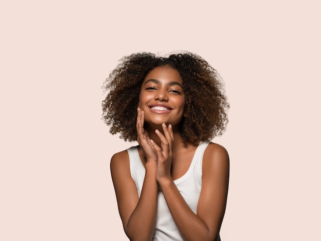 Schöne afrikanische Frau weißes T-Shirt Porträt Afro-Haarschnitt, der ihr Gesicht berührt Farbhintergrund rosa