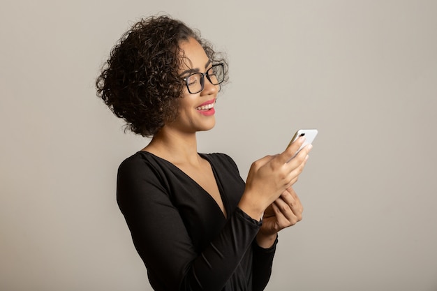 Schöne Afro-Frau lächelnd, Brille tragend und Smartphone verwendend