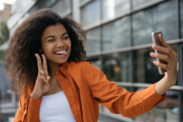 Schöne afroamerikanische Frau, die selfie auf Handy nimmt und Siegeszeichen zeigt. Blogger-Streaming-Video online