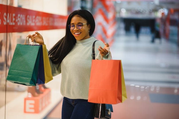 Schöne afroamerikanische Frau mit bunten Einkaufstüten in einem Geschäft.