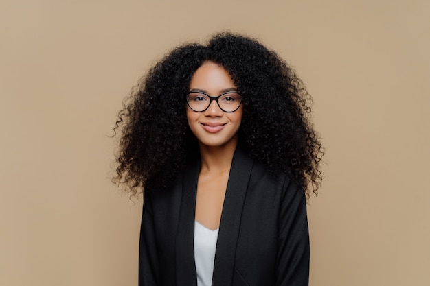 Schöne afroamerikanische Frau mit dem klaren Haar, gekleidet in der eleganten schwarzen Jacke, transparente Gläser