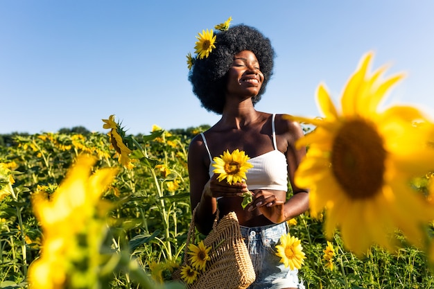 Schöne afroamerikanische Frau mit lockigem Afro-Stil in einem Sonnenblumenfeld