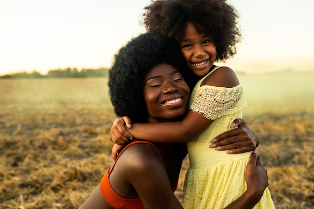 Schöne afroamerikanische Mutter und Tochter, die auf einem Sonnenblumenfeld spielen und Spaß haben