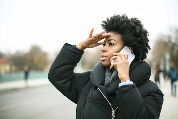 Schöne Afrofrau, die auf einem Smartphone im Freien spricht
