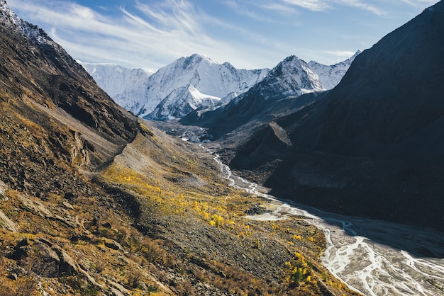 Schöne alpine Landschaft mit großen schneebedeckten Bergen und Bergfluss mit vielen Bächen im Tal zwischen Felsen in Herbstfarbe bei Sonnenschein. Fantastische sonnige Landschaft mit hoher Schneebergwand im Herbst